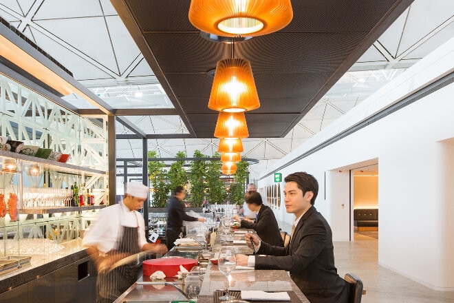 Passengers eating at the bar and chef preparing food at the Qantas Hong Kong lounge