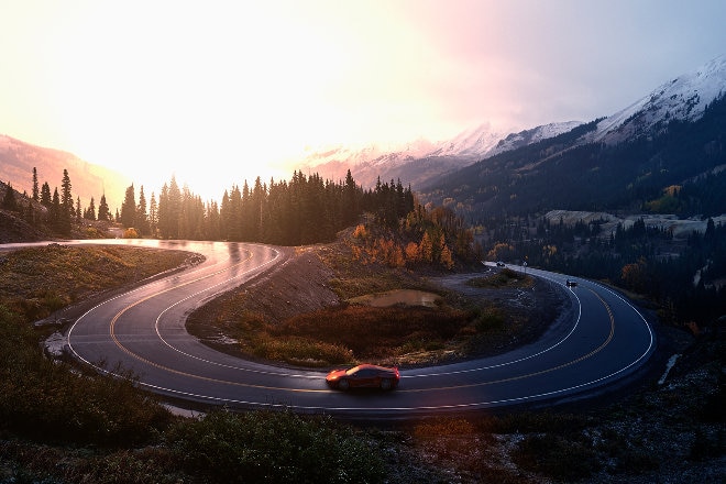 car driving on a windy road through the forest beside snow capped mountains