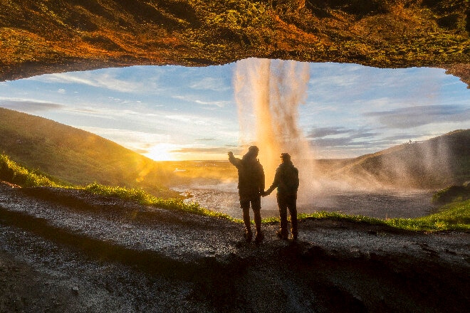 Couple overlooking a waterfall through a rock formation at sunset