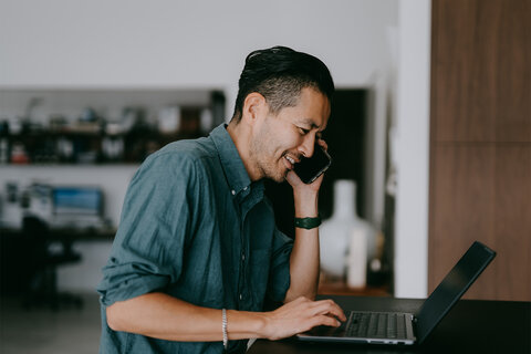 Man smiling while on smartphone and using laptop