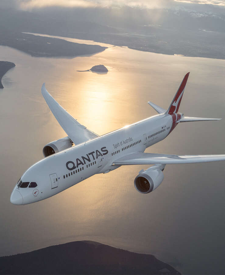 Qantas aircraft flying over coastline at sunset