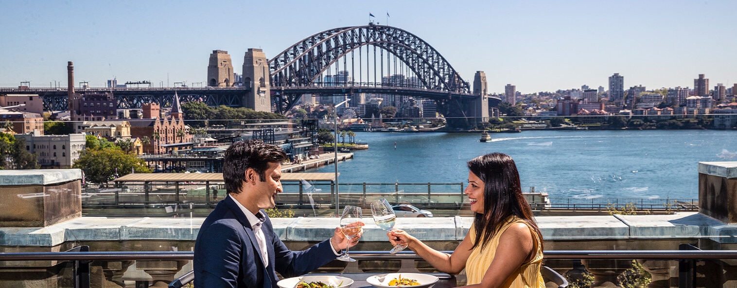 Couple holding drinks in hand together with Sydney Harbour Bridge in the background